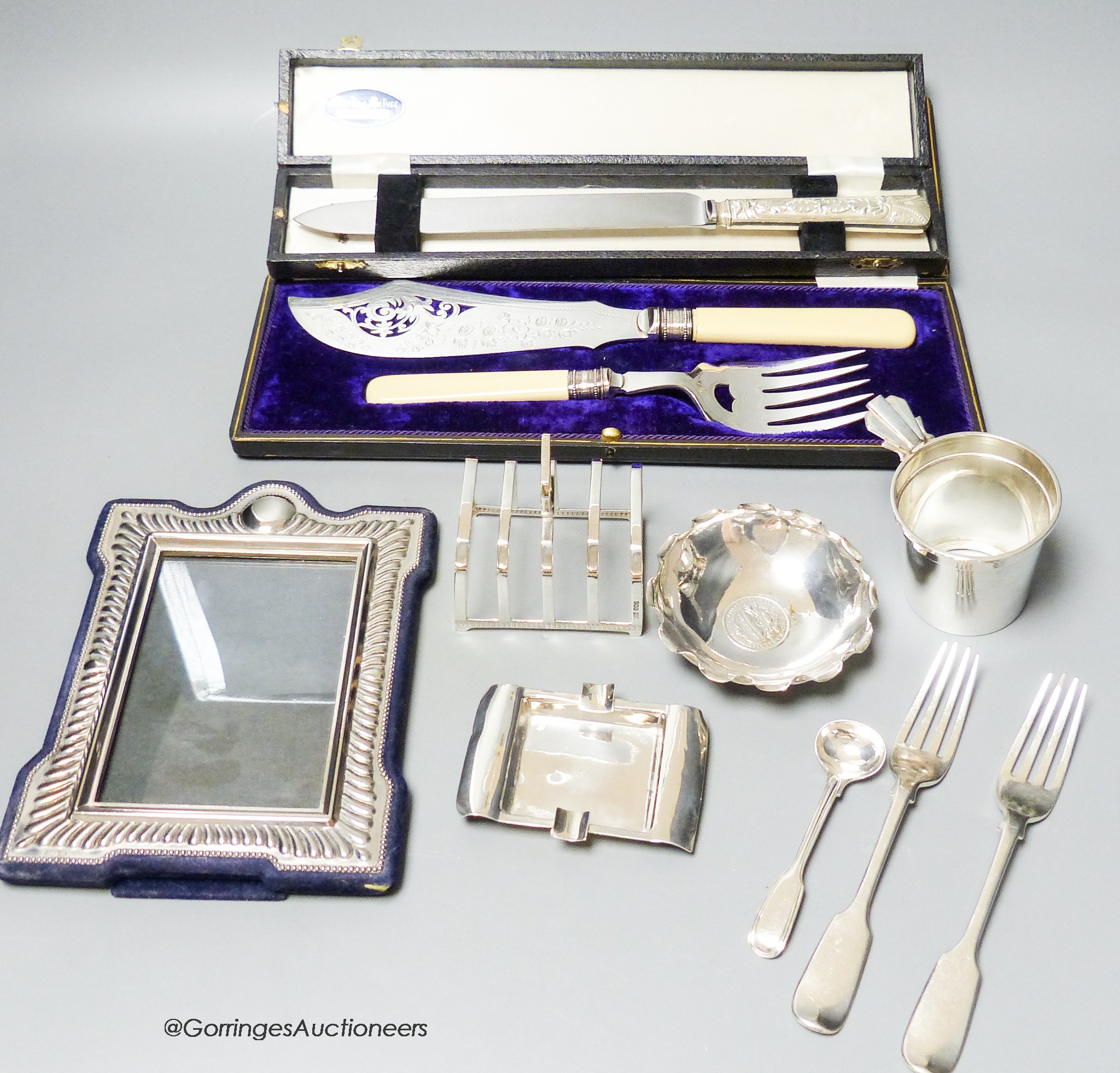 A small group of assorted silver including cup holder, dessert forks, mustard ladle, ashtray, a Wang Hing coin dish and toastrack, (gross 11oz) and three plated items.